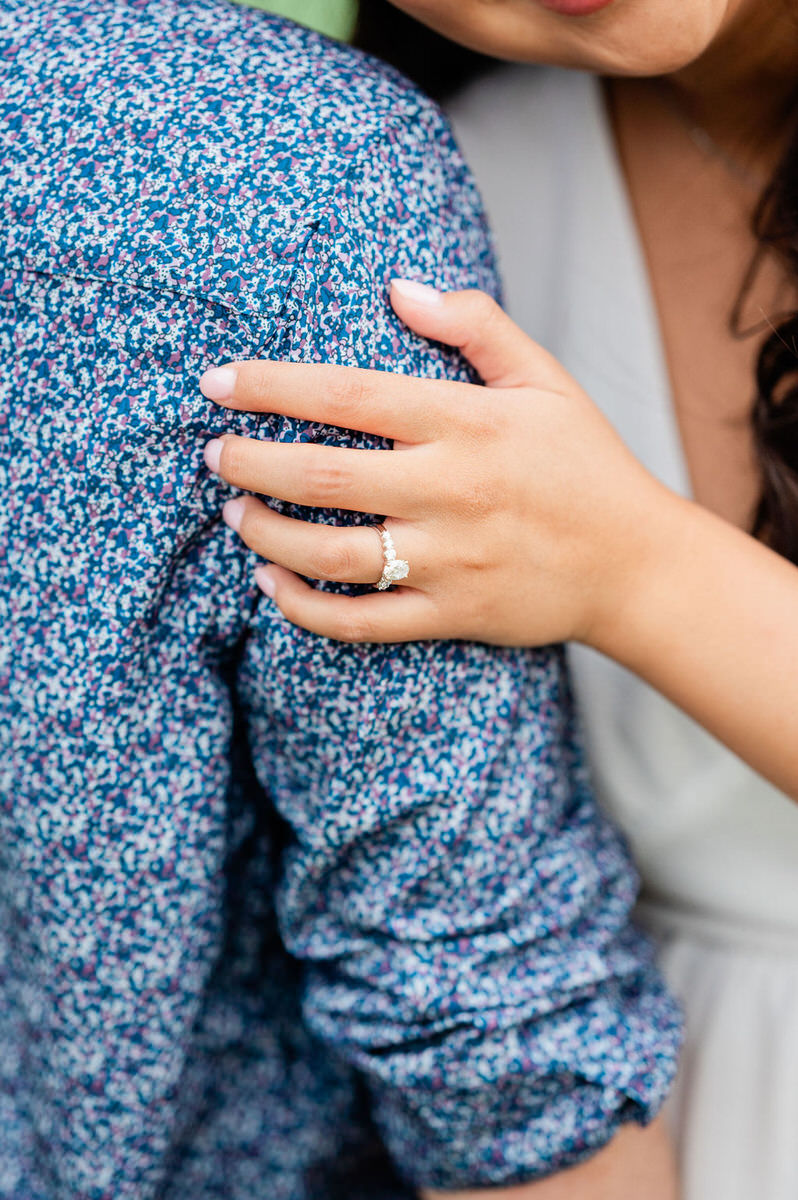 Close-up of a woman's hand on a man's shoulder, showcasing an engagement ring showing off what to wear for engagement pictures.