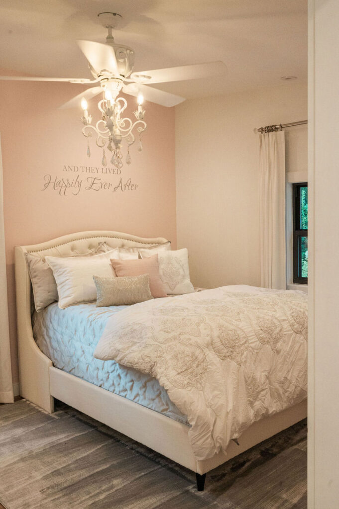 A romantic bedroom with a text "And They Lived Happily Ever After" above the bed, featuring a soft color palette, elegant bedding, and a classic ceiling fan with lighting.