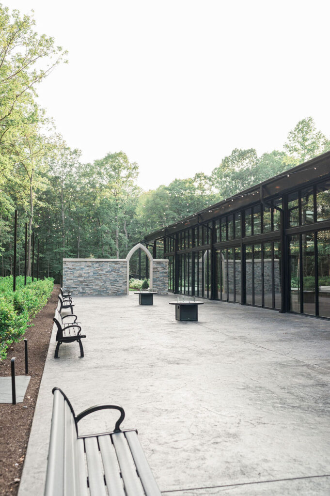 The same outdoor patio viewed from a different angle, showcasing the expansive seating area with benches and the tranquil natural backdrop, perfect for social gatherings.