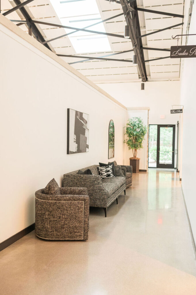 A sleek and contemporary hallway with an industrial ceiling, a comfortable dark textured couch with matching chairs, and modern artwork, providing a sophisticated waiting area.