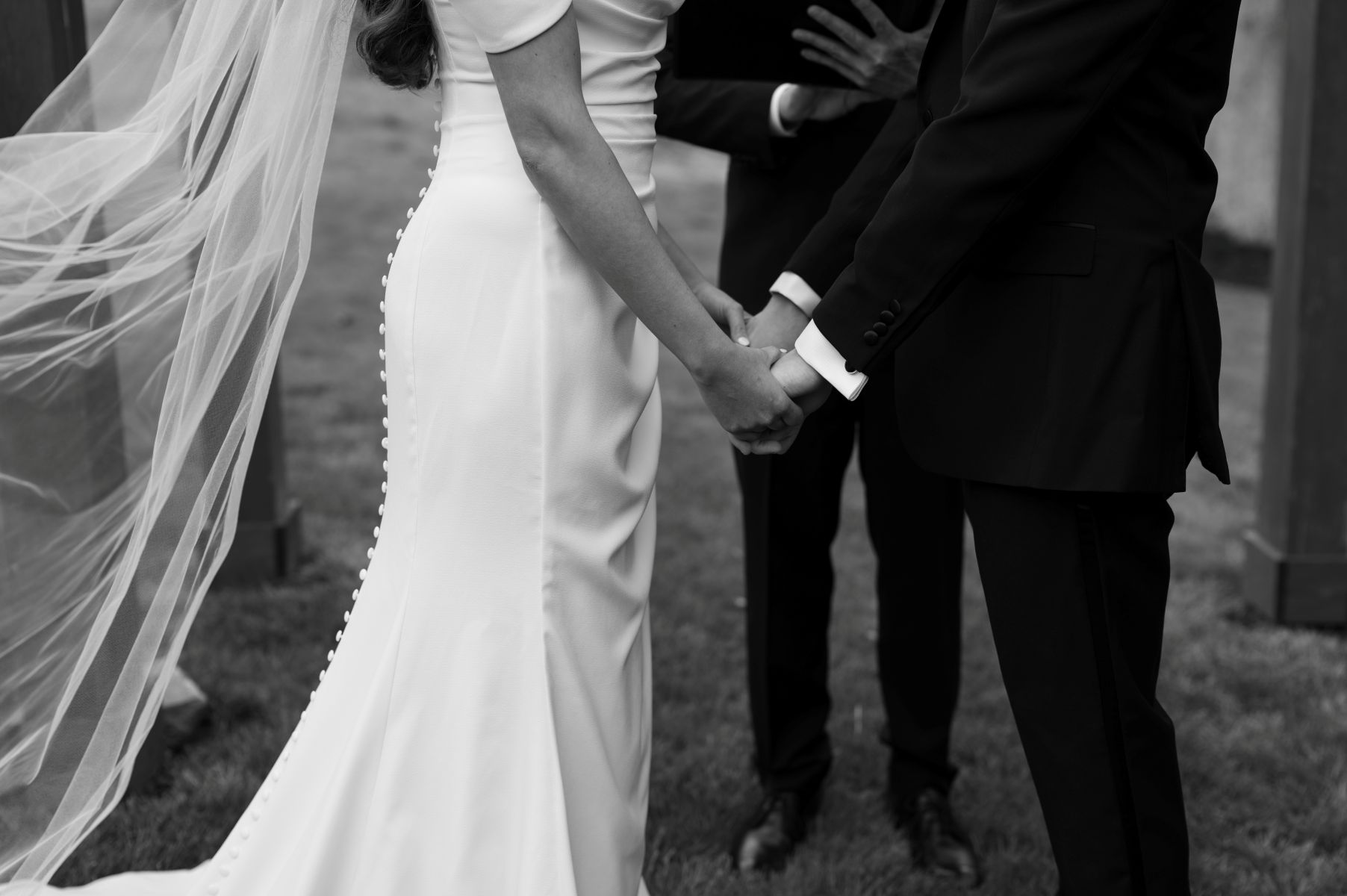 a couple holding hands at their wedding ceremony the woman is wearing a white wedding dress and veil the man is wearing a black tuxedo