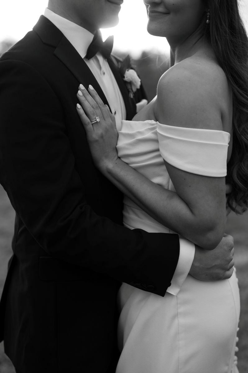 a couple embracing as the sun sets behind them the woman is wearing a white wedding dress the man is wearing a black suit