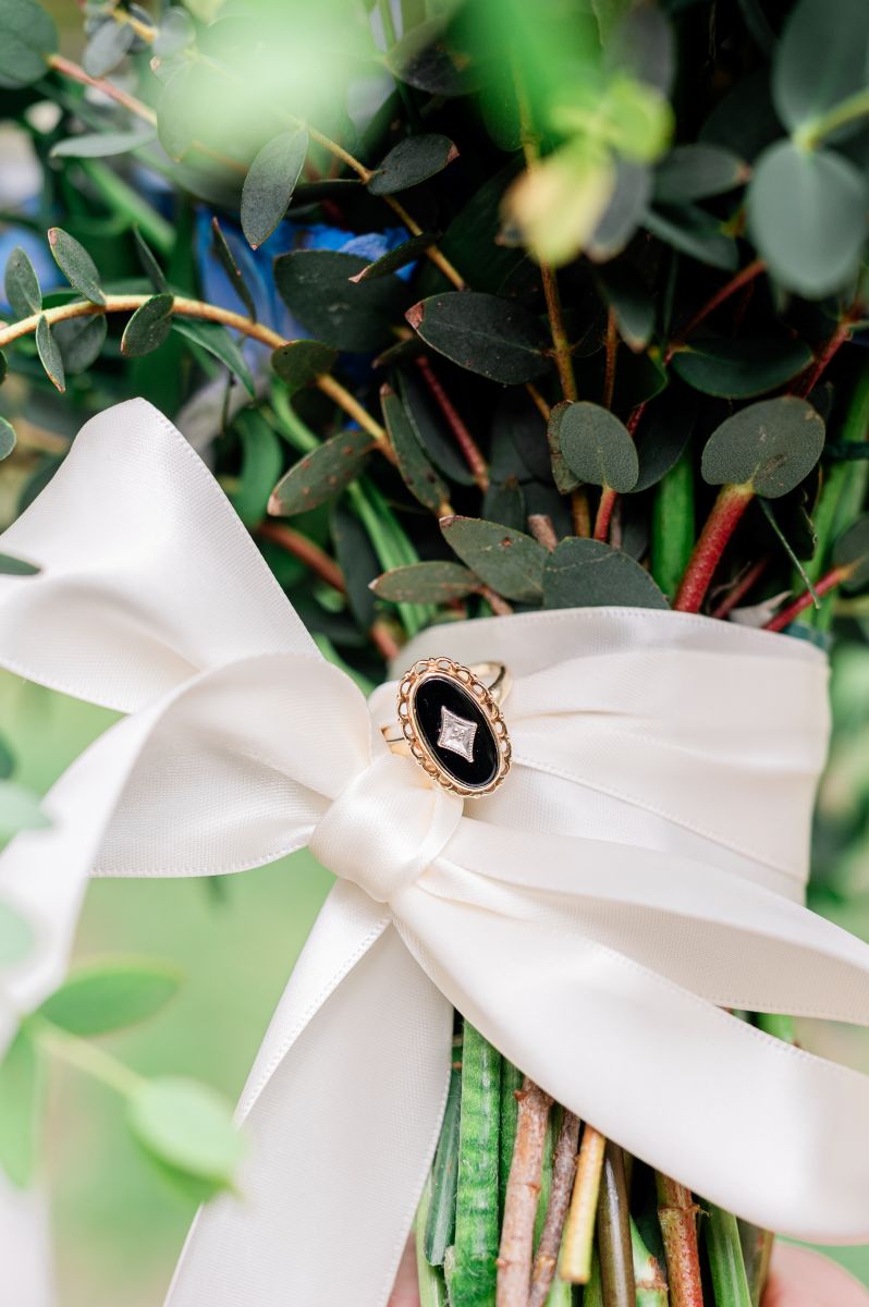a bouquet of flowers wrapped in a white silk bow and with a ring on it
