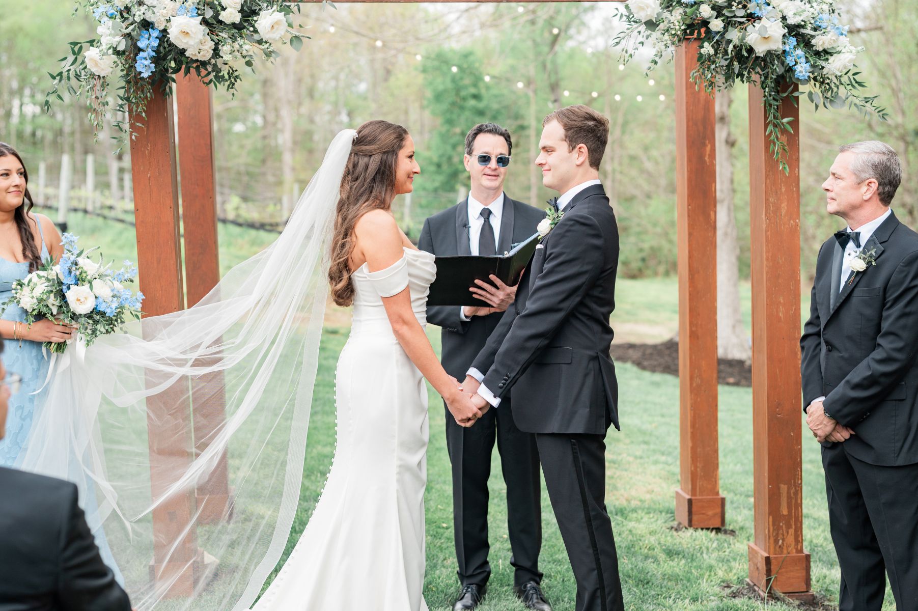 a couple having their wedding at ashton creek vineyard they are holding hands and smiling at each other the woman is wearing a white wedding dress and veil the man is wearing a black suit