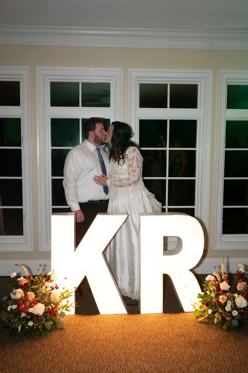 a couple kissing in front of an illuminated k and an illuminated r at their wedding reception