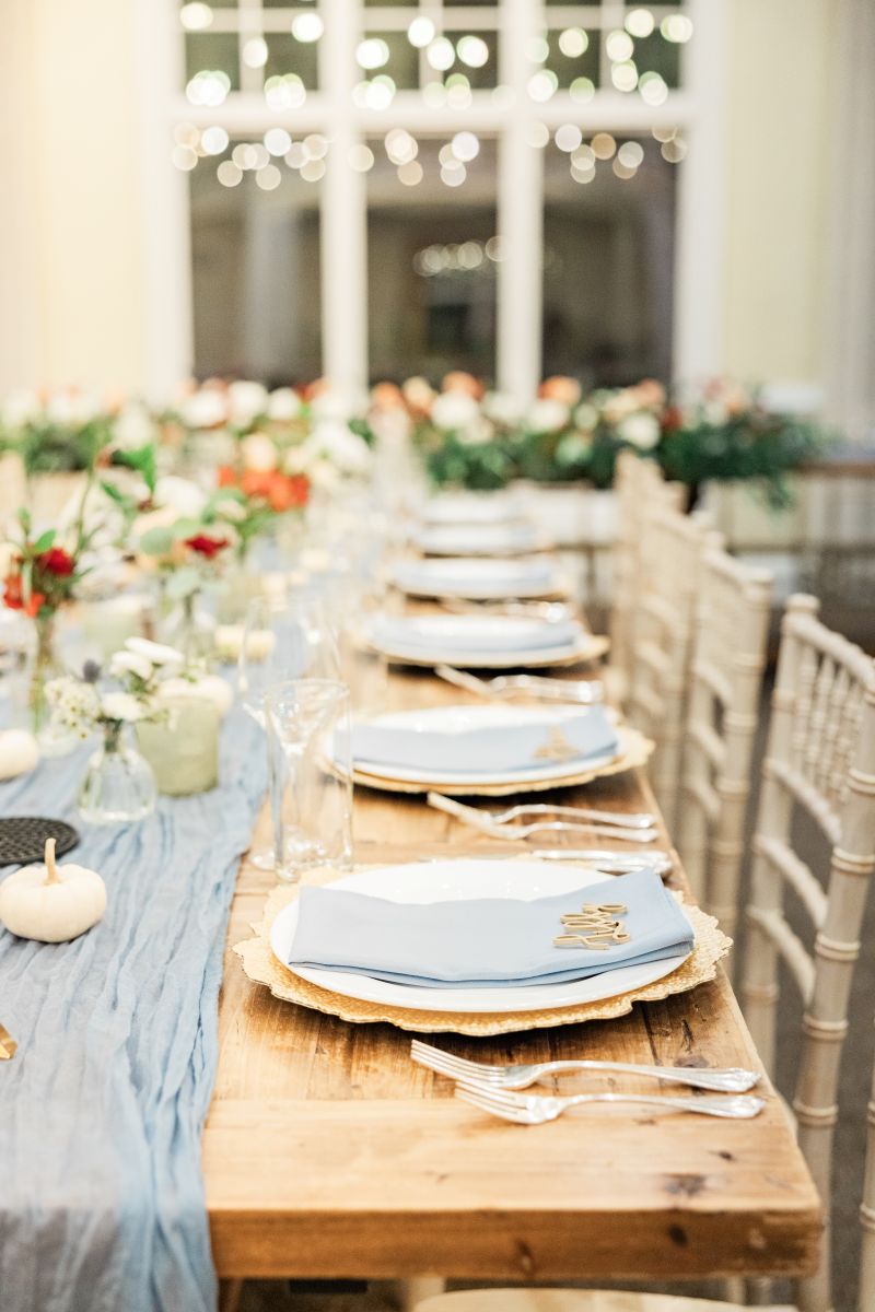 a long wood table elegantly decorated with a tablecloth, flowers, plates, napkins, and silverware