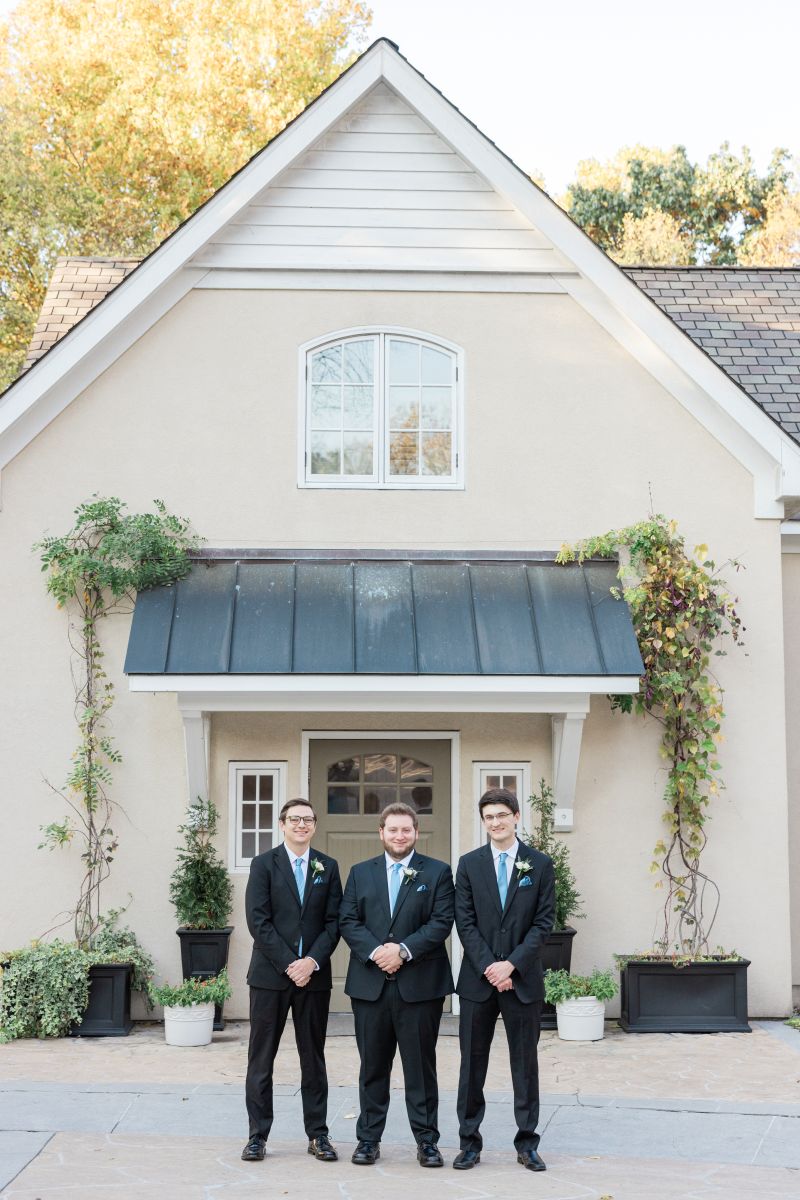 three men wearing black suits and blue ties standing in front of one of the cottages at the mill at fine creek in richmond virginia