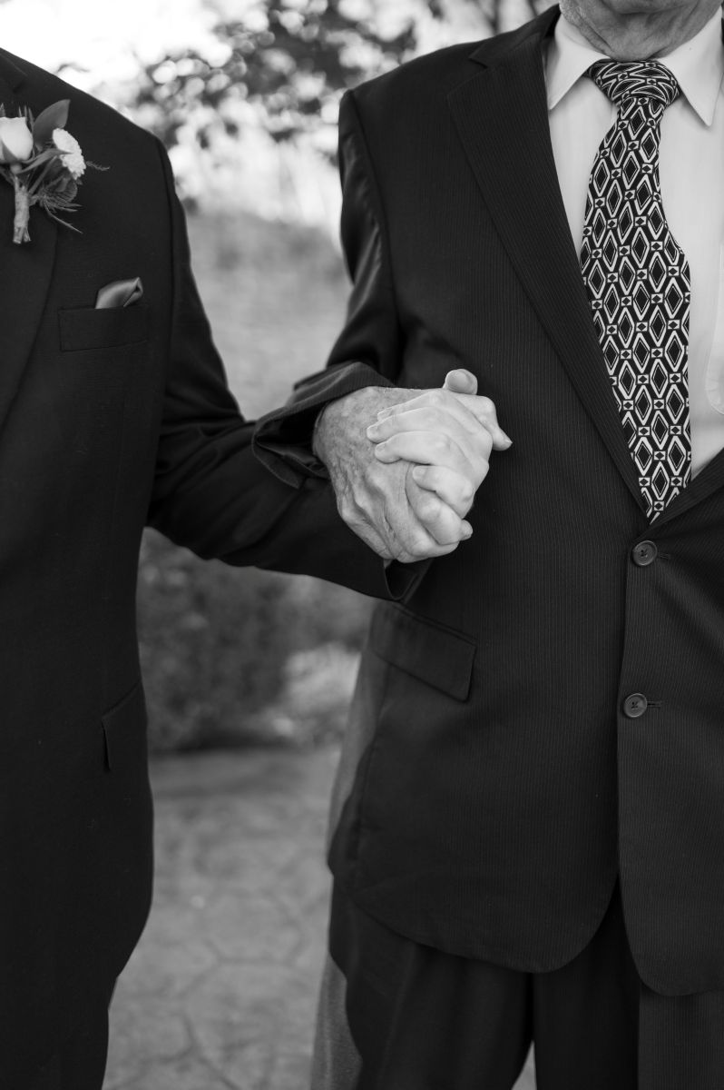 two men holding hands both wearing black suits
