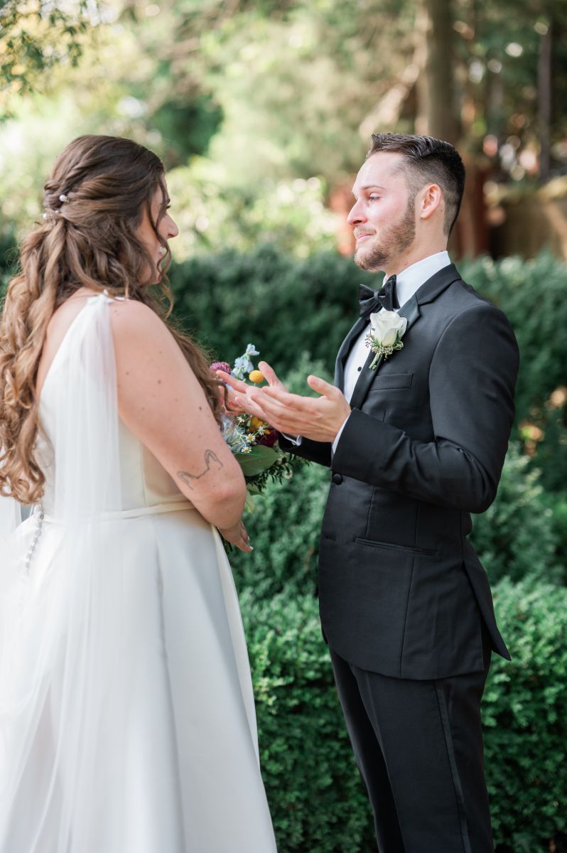 a couple sharing a first look the man is tearful and the woman is wearing a white wedding dress and smiling