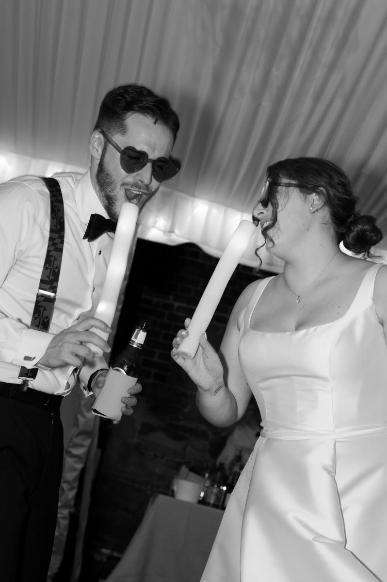 a couple celebrating their wedding underneath a tent they are holding glow sticks and singing to each other