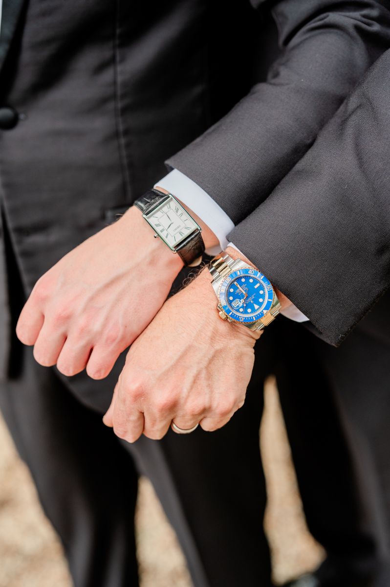 two men both wearing black suits holding up their arms and showing off their wrist watches