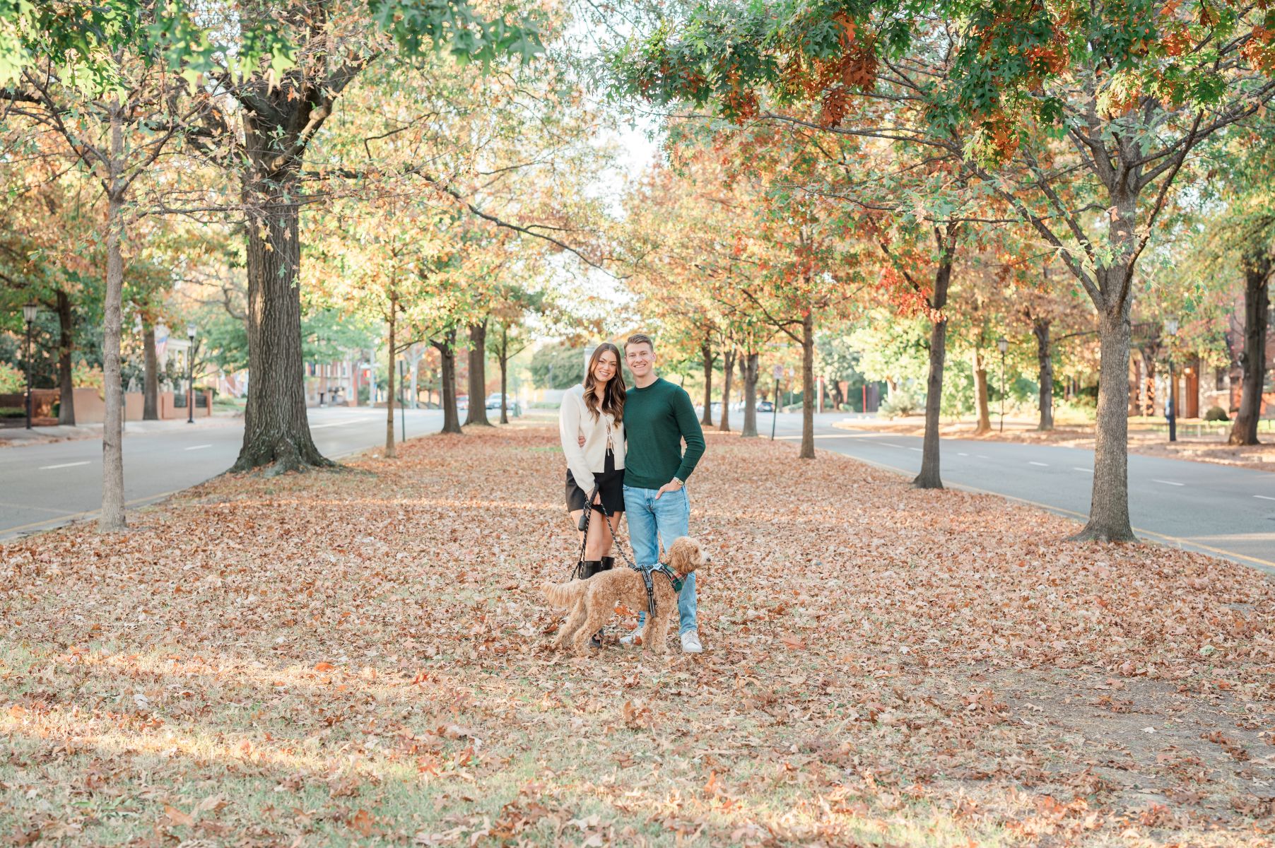 a couple on monument avenue in richmond virginia in the fall they are with their dog and surrounded by fall foliage and trees