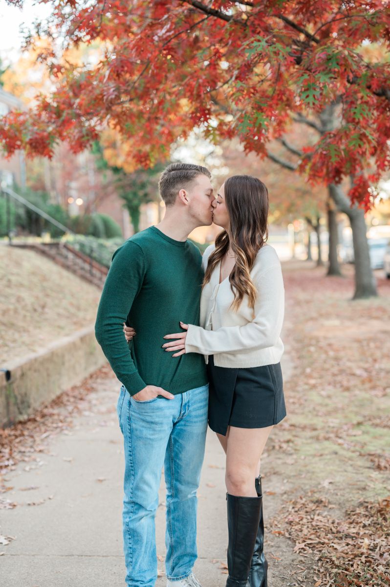 a couple kissing each other on a paved sidewalk surrounded by trees