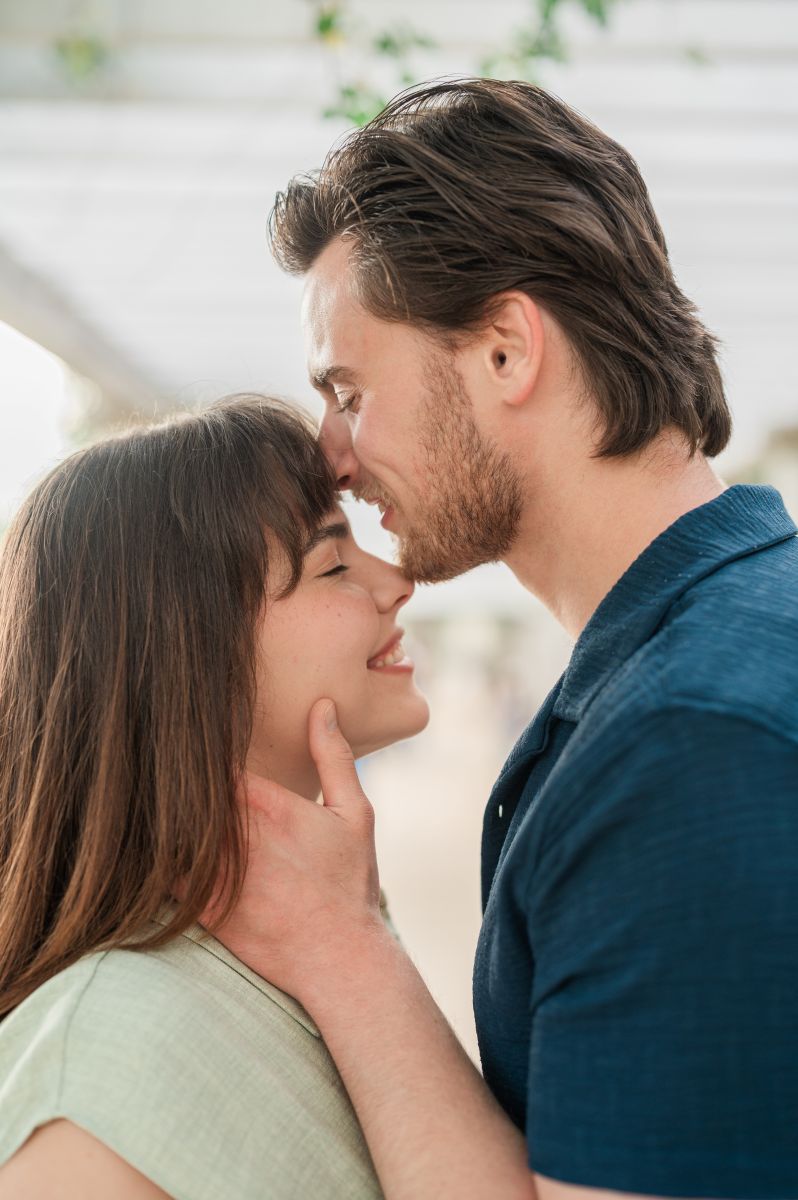 a man with his hands on his partner's next leaning in to kiss her forehead the woman is smiling with her eyes closed