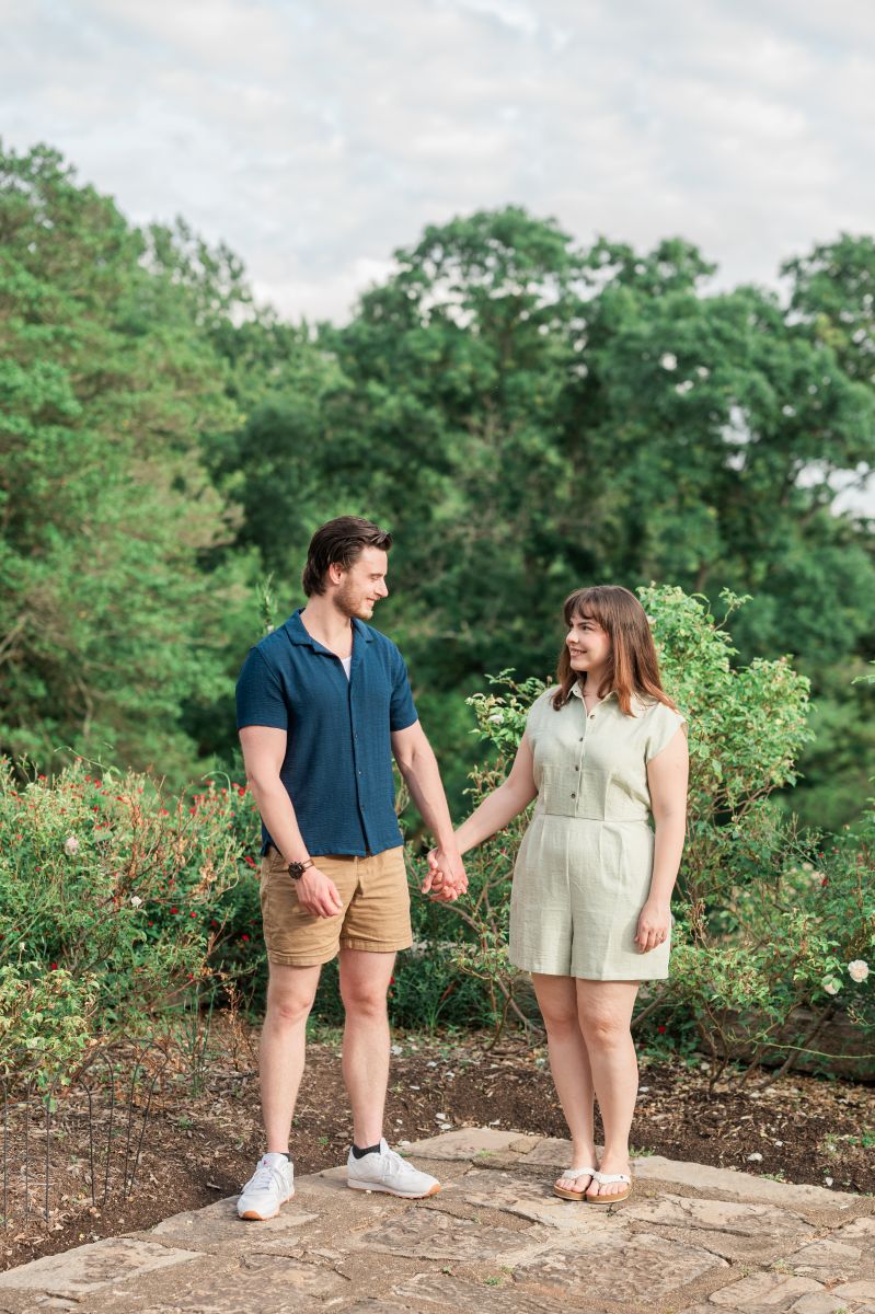 a couple standing next to a garden in maymont park in virgina holding hands and smiling at each other while taking engagment photos